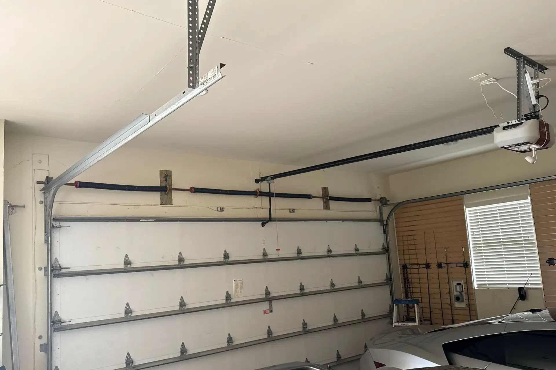 Garage interior with the door open, showing the torsion shaft, drums, cables, tracks and opener rail