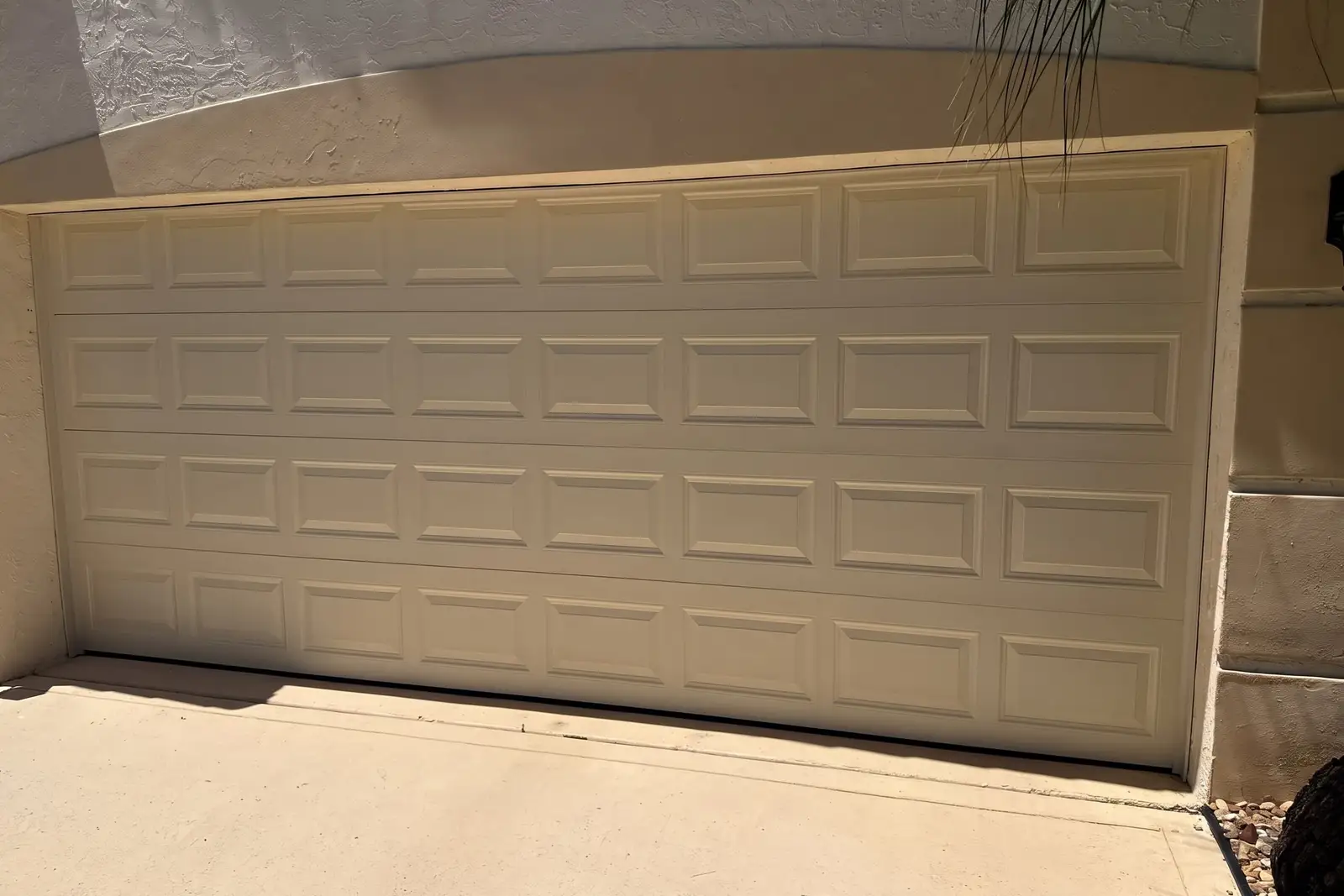 Beige raised-panel double garage door under a curved stucco header