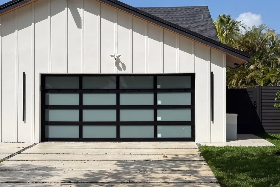 White board-and-batten house with a black-framed frosted-glass garage door, palm trees and a blue sky