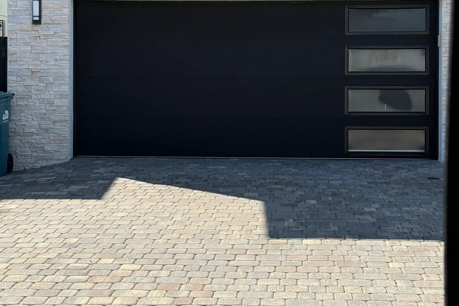 Flush black garage door with a vertical window row on a stone-clad home