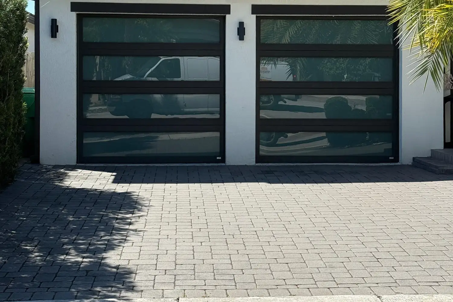 Two dark bronze full-view glass garage doors on a modern stucco home