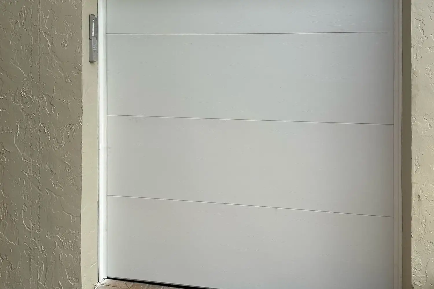 Plain white flush garage door set in a white stucco wall