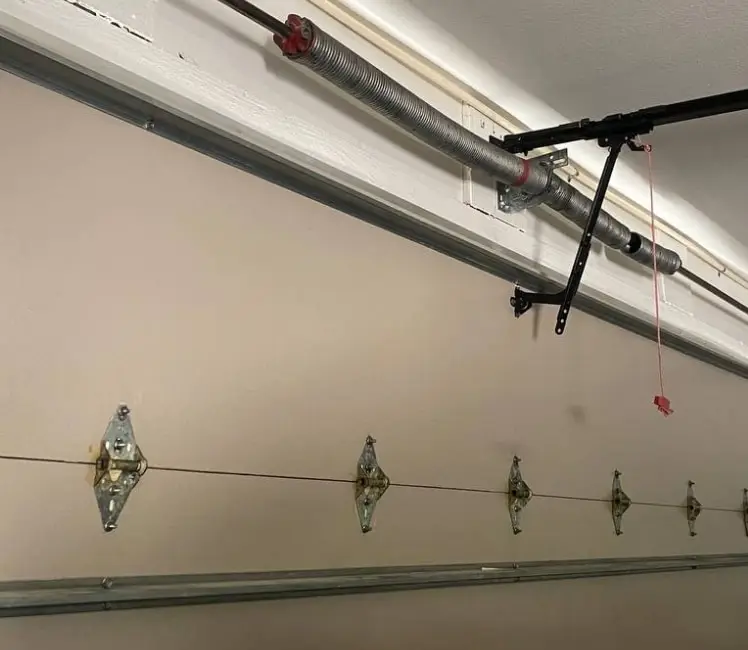 Torsion spring and shaft above a garage door, with the door’s hinges and track below