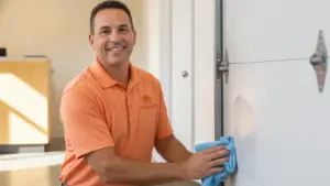 Service professional in orange polo cleaning white garage door with blue cloth.